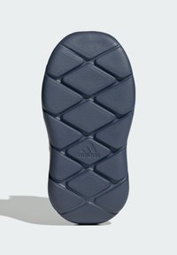 Adidaksen kengän pohja, jossa on tummanharmaata, texturoitua muotoilua, jossa on timanttimäinen kuvio ja logo keskellä. Pyöristetty muoto, jossa on pito-ominaisuuksia.