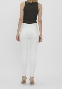 Jean skinny blanc à taille haute avec poches arrière, associé à un débardeur noir côtelé et des chaussures à talons beiges.