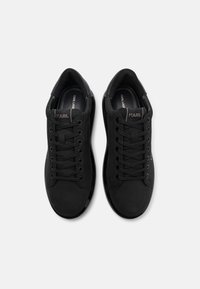 Juodos sportinės bateliai su lygiu odiniu viršumi, plokščiomis raištelėmis ir tekstūruotu guminiu padu. Ant liežuvio yra logotipas, skirtas prekės ženklui.