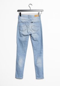 Jeans ajustados de color azul claro, confeccionados en denim, con una cintura de altura media, bolsillos traseros y un ligero desvanecimiento cerca de las rodillas, colgados de una percha negra.