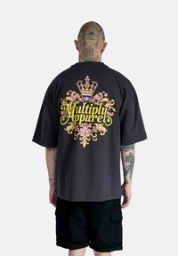 Camiseta negra de manga corta con un gráfico colorido de estilo barroco que presenta una corona y el texto "Multiply Apparel" en la parte posterior.
