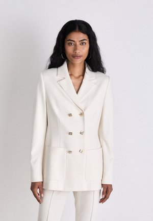 Doppelreiher-Blazer aus cremfarbener Stoff mit goldfarbener Hardware, Schalkragen und zwei Fronttaschen in taillierter Passform.