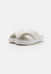 Vita crossover-slide sandaler med en mjuk, vadderad yta, utrustade med en tjock vit sula och en minimalistisk design.
