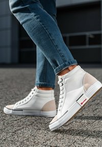 Zapatillas altas de cuero blanco con acentos de ante beige, que cuentan con una suela texturizada y una etiqueta de marca roja en el lateral.