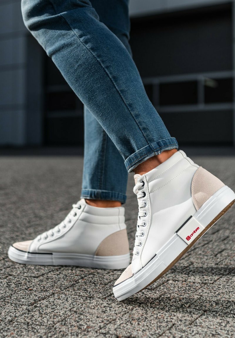 Zapatillas altas de cuero blanco con acentos de ante beige, que cuentan con una suela texturizada y una etiqueta de marca roja en el lateral.