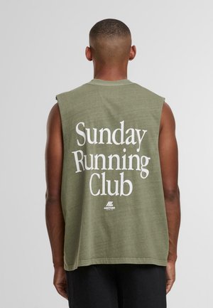 Man met kort haar, gekleed in een mouwloos olijfgroen shirt met "Sunday Running Club" in het wit op de achterkant.