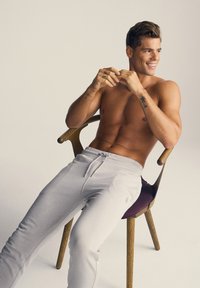 Lysegrå sweatsbukser med snøring, glat tekstur og slim fit, båret af en person, der sidder i en træstol med burgunderfarvet accent.