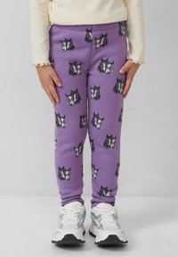 Fioletowe legginsy z powtarzającym się wzorem czarnych i szarych psów, wykonane z miękkiego, elastycznego materiału w dopasowanym kroju. W zestawie z białymi sneakersami.