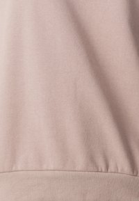 Tejido de sudadera de color rosa claro con textura suave. Cuenta con una cintura acanalada. El diseño general es minimalista y sencillo.
