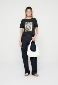 Zwarte t-shirt met een zilveren pailletten rechthoekig patroon, gecombineerd met donkerblauwe wijde jeans en een witte handtas met studaccenten.