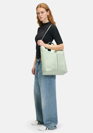 Borsa tote in pelle verde con forma oversize, doppi manici e cuciture a scomparsa. Indossata con denim morbido e sneakers per un look casual.