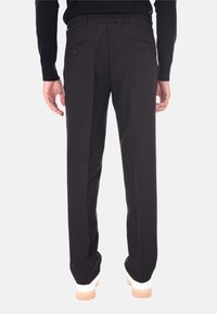Vista posteriore di una persona che indossa pantaloni neri su misura con tasche posteriori abbottonate e sneaker bianche con suola in gomma.