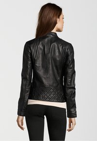 Black leather jacket with a fitted design, quilted texture at the back hem, and a stand collar. Long sleeves with stitched detailing.