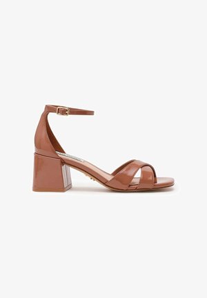 Sandale en cuir verni marron avec talon bloc, bride à la cheville, bout ouvert et deux brides croisées sur le dessus du pied.