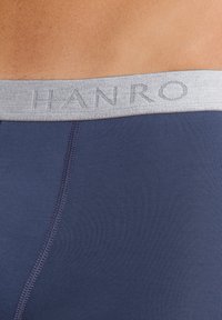 Navyblå kalsonger med en ljusgrå elastisk midjeband som har präglad "HANRO"-branding. Slät textur och figurnära design.