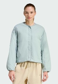 Svetlo modrá prešívaná bunda s okrúhlym výstrihom, dlhými rukávmi a predným zapínaním na patentky. Materiál má hladkú, jemne zvrásnenú textúru.