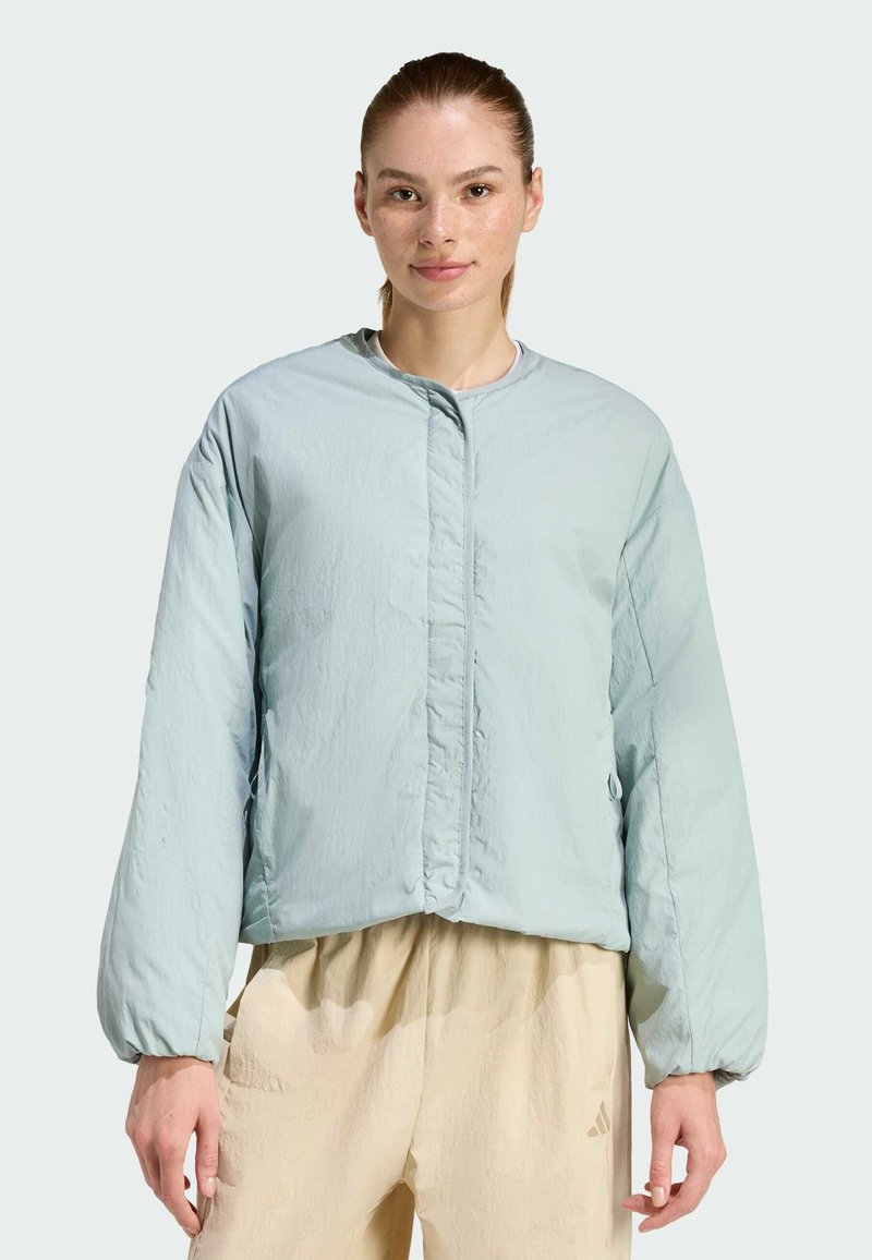 Svetlo modrá prešívaná bunda s okrúhlym výstrihom, dlhými rukávmi a predným zapínaním na patentky. Materiál má hladkú, jemne zvrásnenú textúru.