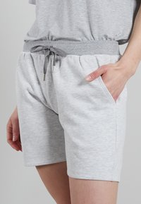 Hnedé šortky z bavlnenej zmesi s elastickým pásom a nastaviteľnou šnúrkou. Obsahujú bočné vrecká a majú hladkú, jemnú textúru.