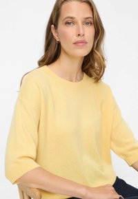 Pull en maille jaune clair à coupe décontractée, manches courtes et encolure arrondie. Texture douce et coutures minimales accentuent le design.