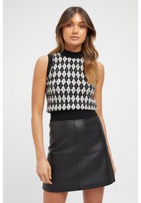 Black and white diamond-patterned knitted sleeveless top with a round neckline, paired with a fitted black leather mini skirt.