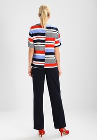 Korte mouwen top met horizontale en verticale strepen in rood, blauw, zwart en wit, gecombineerd met marineblauwe wijde broek en rode hakken.