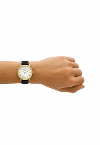 Guldtonad klocka med en vit snäcka urtavla, svart läderrem och romerska siffror, visad på en hand.