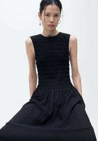 Abito nero senza maniche con corpino arricciato, gonna fluida e texture liscia. Design semplice senza motivi o decorazioni visibili.