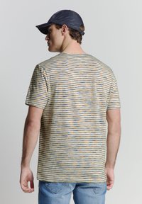 T-shirt en coton rayé avec des lignes horizontales jaunes, bleues et blanches. Manches courtes et col rond. Porté avec un jean en denim.