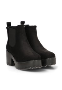 Botas de tobillo de ante negro con suela gruesa, paneles laterales elásticos y tira de agarre; presentan una textura suave y un diseño de punta redondeada.