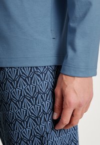 Haut bleu à manches longues avec une texture côtelée, associé à un pantalon bleu foncé à motifs présentant un design géométrique avec des accents bleu clair.