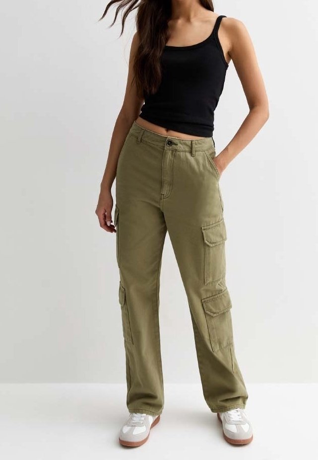 Groene cargobroek met meerdere zijzakken, gemaakt van stevige stof. Gepaard met een zwart tanktop en witte sportschoenen.