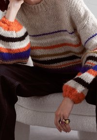 Pull en tricot avec des rayures horizontales orange, bleu, marron et noir. Caractérisé par un fil épais et texturé ainsi que des manches surdimensionnées.