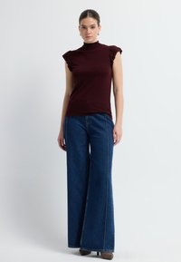 Top burdeos sin mangas con hombros con volantes, combinado con jeans de mezclilla azul de pierna ancha y tiro alto, y zapatos de tacón marrones.