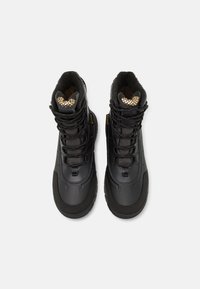 Schwarze wasserdichte Stiefel mit einem schlichten Design, ausgestattet mit Gummisohlen, strukturiertem Obermaterial und mit goldenen Akzenten versehenen Einlegesohlen. Mit verstellbaren Schnürungen.