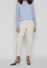 Svetlemodrá blůza s chevronovým vzorem, elastické manžety; krémové tapered kalhoty; černé lodičky na podpatku se zdobnou embellishment.