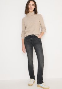 Suéter de cuello alto texturizado en color beige combinado con jeans ajustados de color gris oscuro. El modelo lleva zapatillas blancas con detalles en azul. Diseño sencillo, apariencia casual.