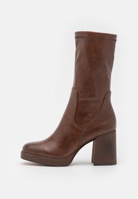 Bottine en cuir marron avec un haut talon bloc, texture lisse, bout rond et panneaux latéraux élastiques pour un enfilage facile.