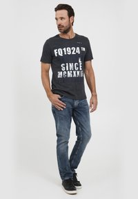 T-shirt in cotone grigio scuro con stampa in bianco audace, abbinato a jeans in denim blu a lavaggio medio e sneakers nere. Vestibilità casual.
