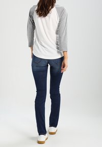 Weißes und graues Oberteil mit drei Viertelärmel und blauen Jeans. Das Oberteil hat einen runden Halsausschnitt und eine lockere Passform, während die Jeans enganliegend sind und Gesäßtaschen haben.