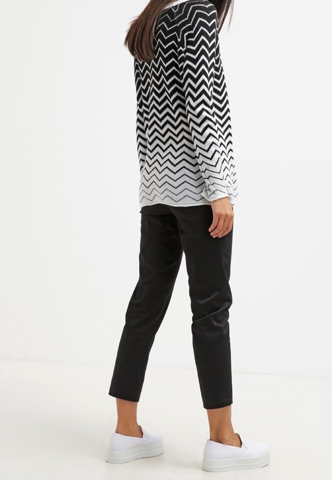 Pull en tricot noir et blanc à motif en chevrons, associé à un pantalon noir et des baskets compensées blanches. Le pull présente des manches longues et une finition texturée.