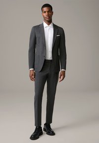 Szary garnitur o dopasowanym kroju, zestawiony z białą koszulą z guzikami. Warto zwrócić uwagę na szczegóły, takie jak poszetka i czarne buty.