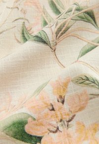 Bloemstoffen met een lichte beige achtergrond, met zachte roze en gele bloemen en groene bladeren, een gestructureerde weving en subtiele patroondetails.