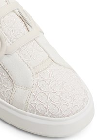 Weißer Sneaker aus strukturiertem Stoff mit einem geprägten Herzmotiv, runder Zehenpartie und flacher Sohle. Enthält einen auffälligen Riemen und eine Schnalle.