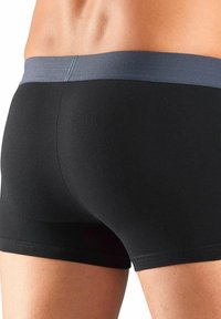 Crne rastezljive tkanine bokserice sivoj elastičnoj uvojnoj traci, ističući prilagođen dizajn i glatku teksturu.