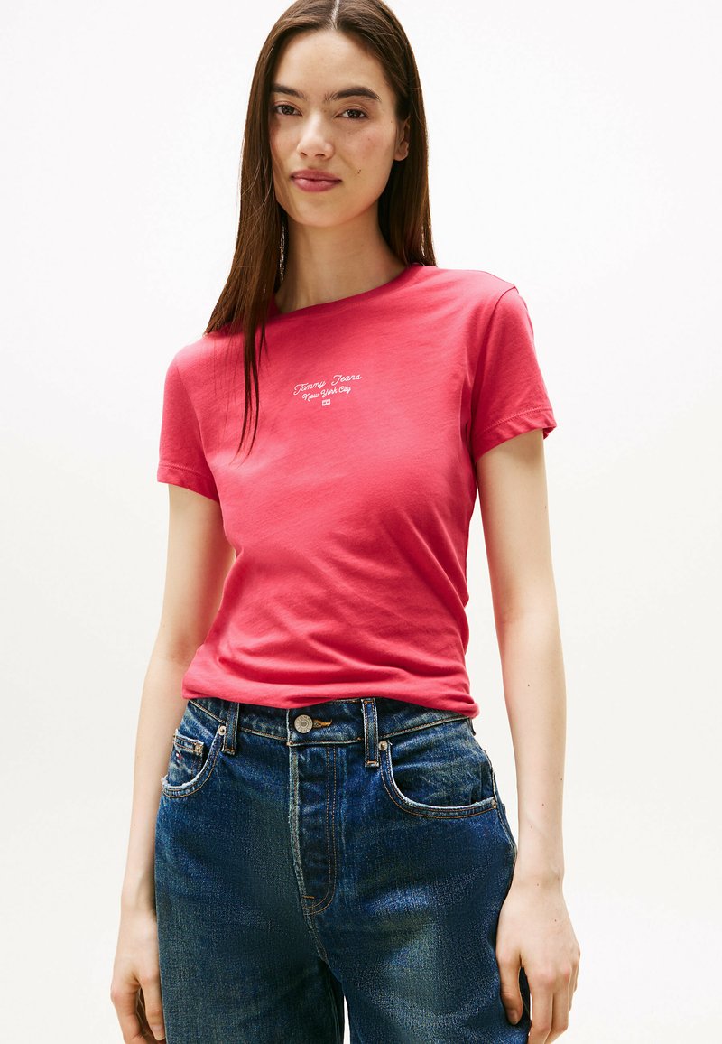 Camiseta de algodón roja con mangas cortas que presenta texto bordado en blanco. Combinada con vaqueros de tiro alto azules, que muestran un ajuste relajado y un diseño clásico.