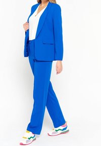 Modrý elegantní oblek s jednou knoflíkovou blazer a rovnými nohavicemi. Nosit s bílým topem a vícebarevnými sportovními teniskami.