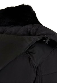 Svart puffjakke med faux fur krage, med glidelåsåpning og glatt, kviltet tekstur. Justeringshardware synlig inne.