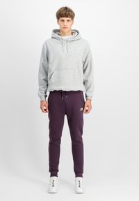 Grauer Kapuzenpullover mit einer Fronttasche, kombiniert mit dunkelvioletten Jogginghosen mit elastischem Bund und Logodetail. Weiße Sneaker.