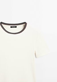 T-shirt crème à côtes avec un col rond, présentant une bordure contrastante en rayures noires et rouges. Manches courtes avec une coupe standard.