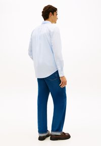 Ανοιχτό μπλε πουκάμισο με καρό μοτίβο, μακριά μανίκια, μανσέτες με κουμπιά, πτυχές στην πλάτη· συνδυασμένο με τζιν μπλε με ίσια γραμμή και καφέ παπούτσια.